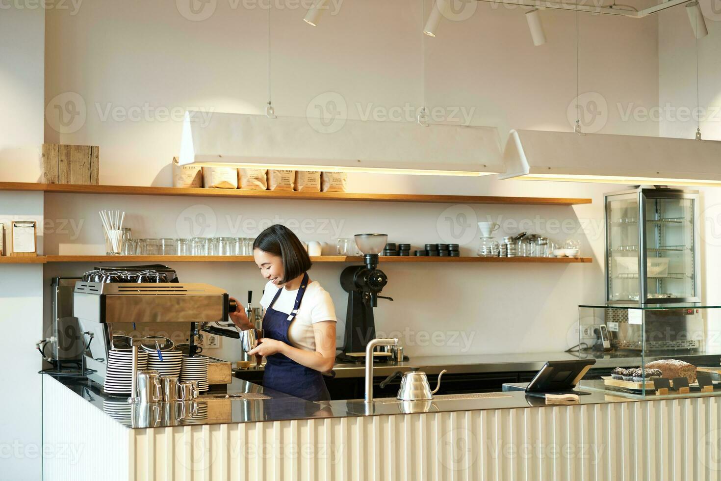 retrato do cafeteria contador com barista menina trabalhando com café máquina, fazer ordem para cliente dentro comprar, vestindo azul avental foto