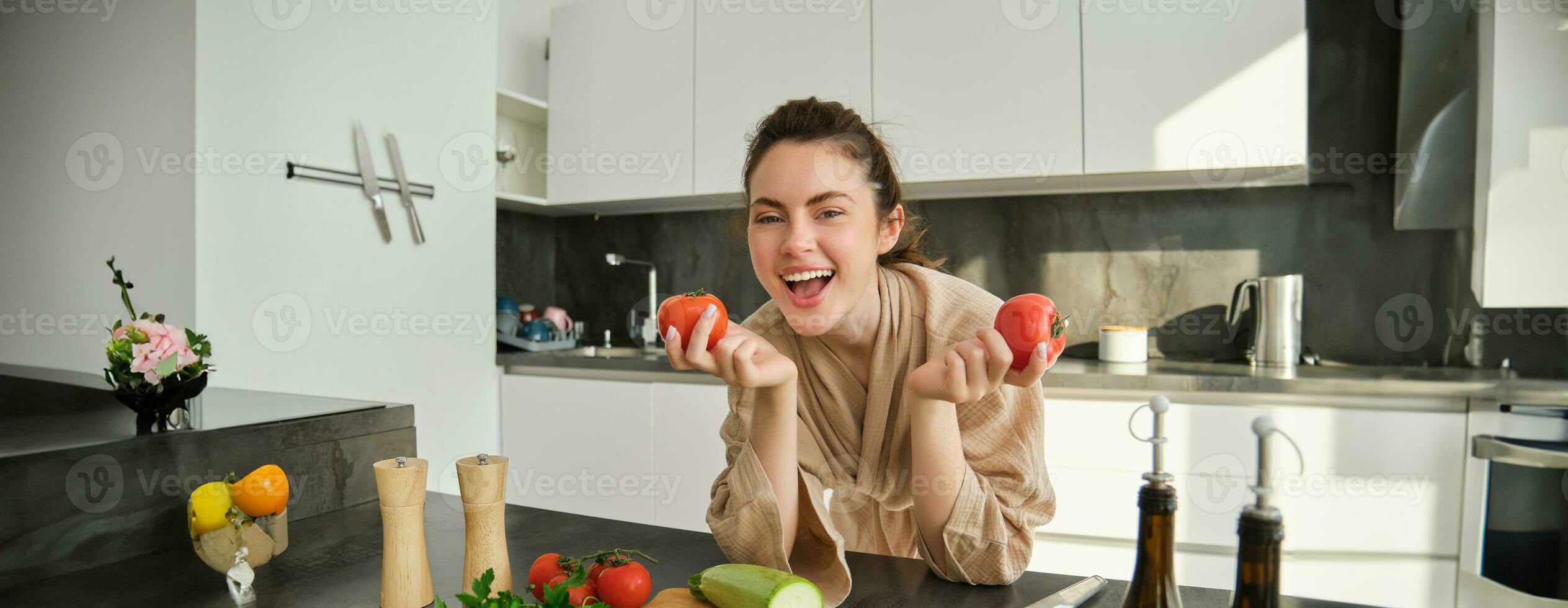 retrato do lindo mulher cozinhando dentro a cozinha, cortar legumes em quadro, segurando tomates, conduzir saudável estilo de vida com preparando fresco saladas, vegano refeições foto