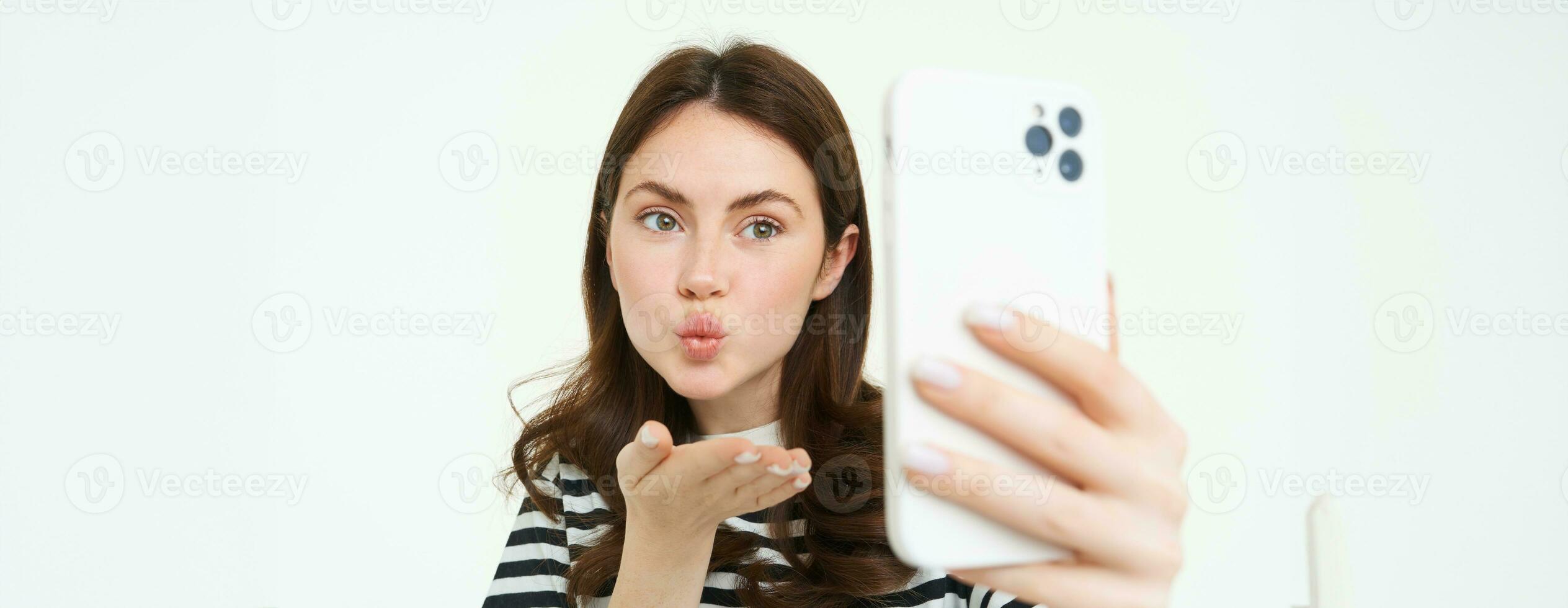 retrato do jovem europeu mulher levando selfie em Smartphone, segurando branco Móvel telefone e posando para fotos, isolado contra branco fundo foto