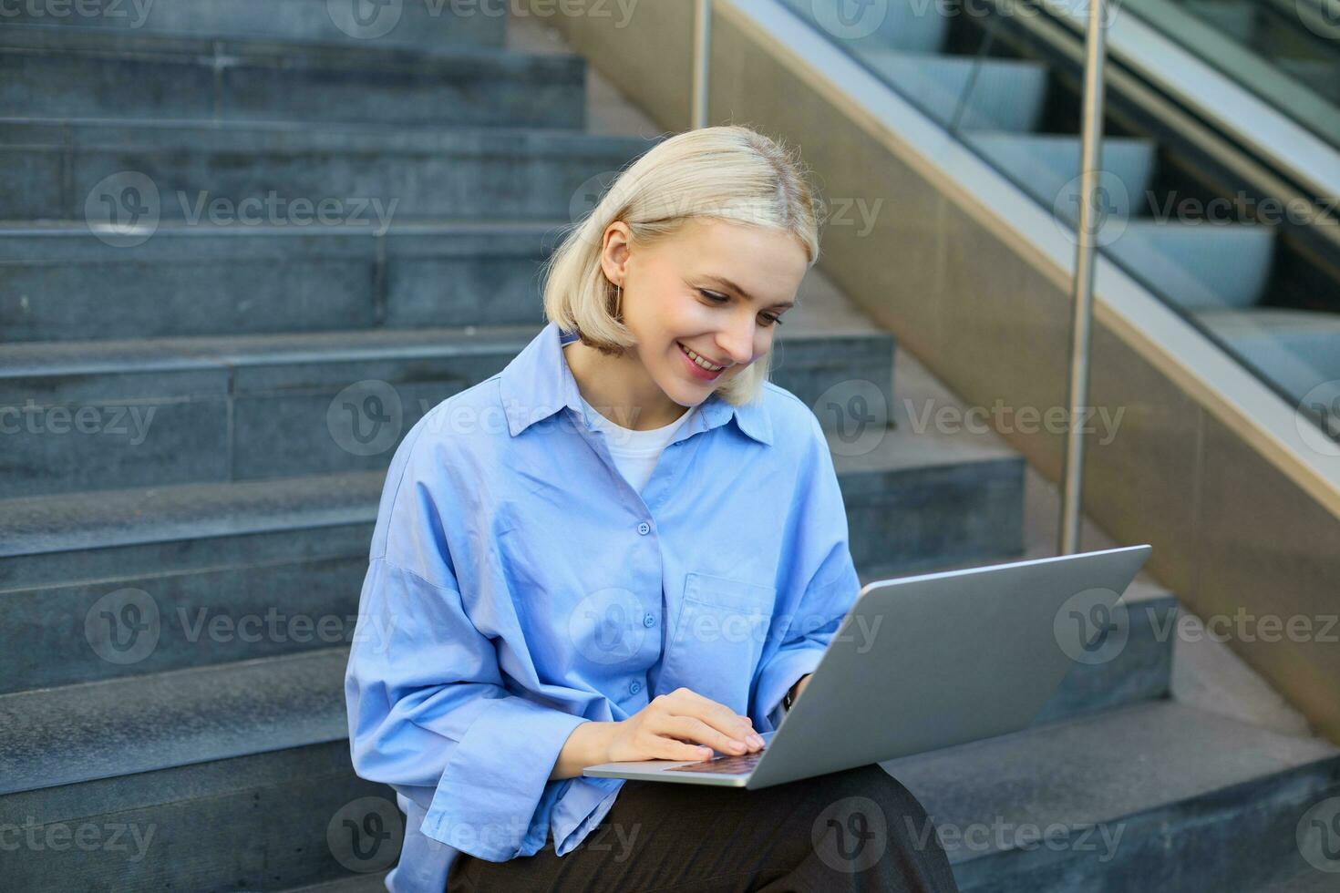sorridente menina aluna usando computador portátil computador moderno tecnologia dispositivo ao ar livre dentro universidade campus conectados aprendizado, elearning lado de fora sentado em urbano escadaria. rede Educação curso webinars conceito foto