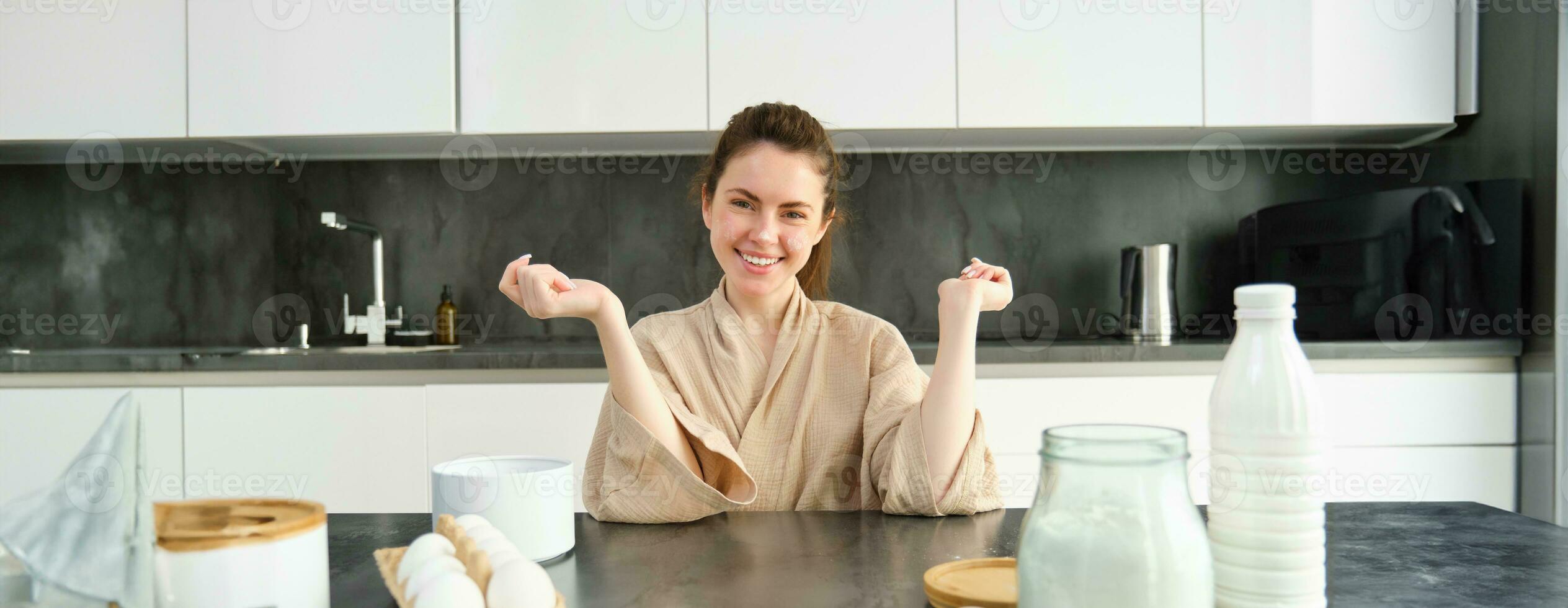 atraente jovem alegre menina cozimento às a cozinha, fazer massa, segurando receita livro, tendo Ideias foto