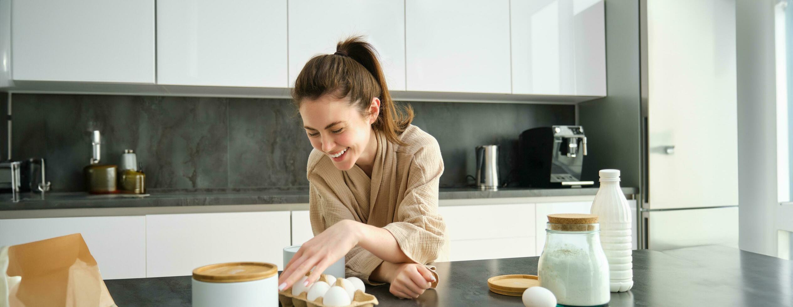 atraente jovem alegre menina cozimento às a cozinha, fazer massa, segurando receita livro, tendo Ideias foto