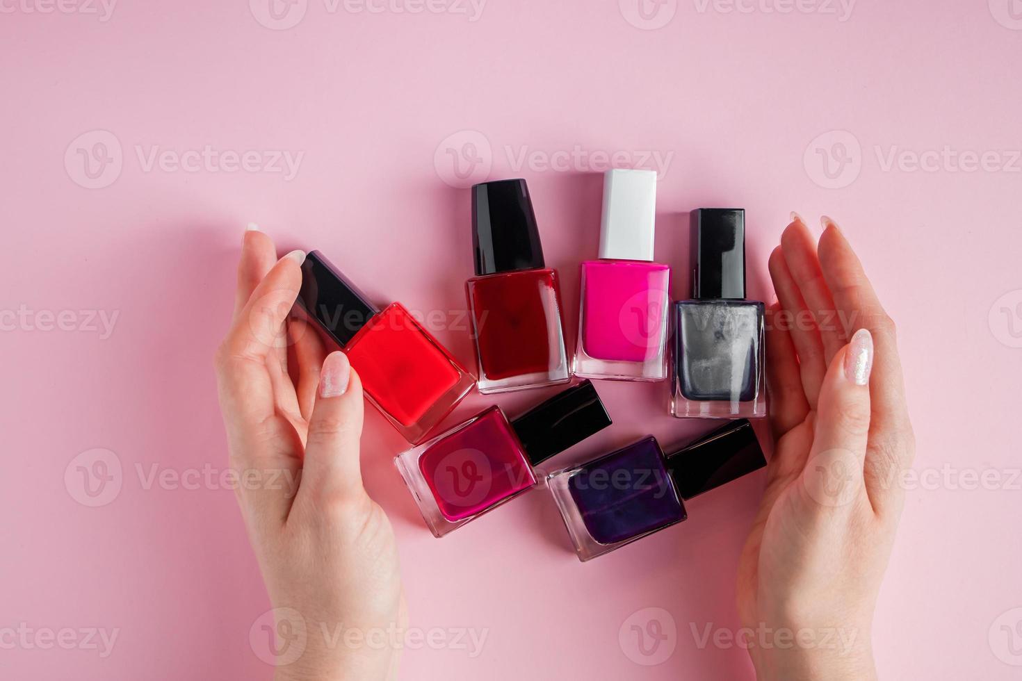 mãos femininas com esmaltes brilhantes. um grupo de esmalte colorido sobre fundo rosa. foto