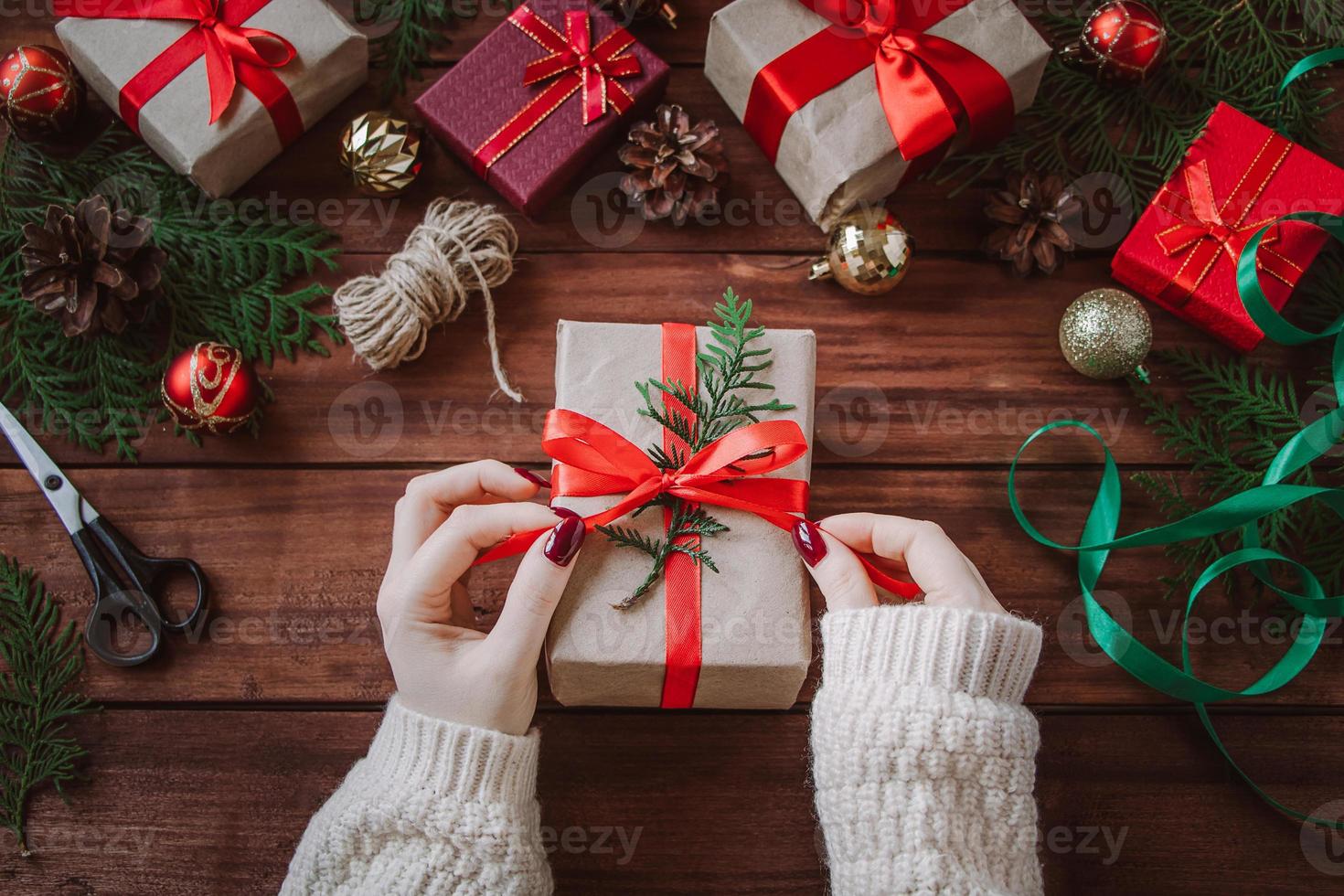 processo de embrulho de presente de Natal. mulher decora a caixa com fita vermelha. foto