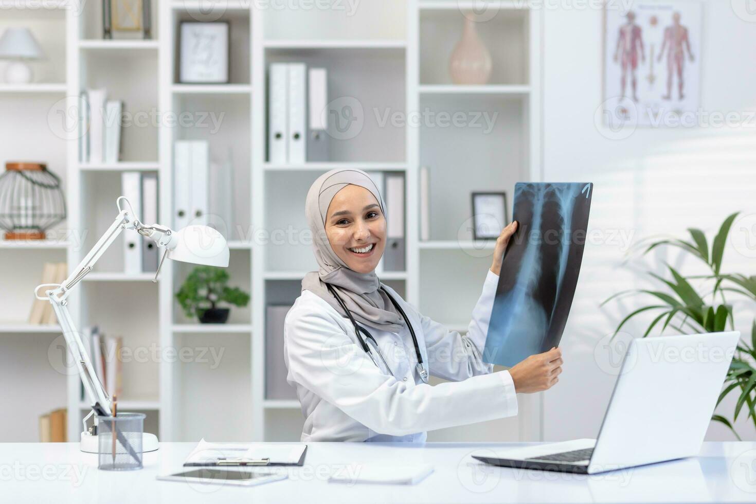 árabe muçulmano mulher médico sentado às mesa dentro escritório dentro privado clínica segurando raios X dentro mãos conduzindo consulta sorridente olhando às Câmera. foto