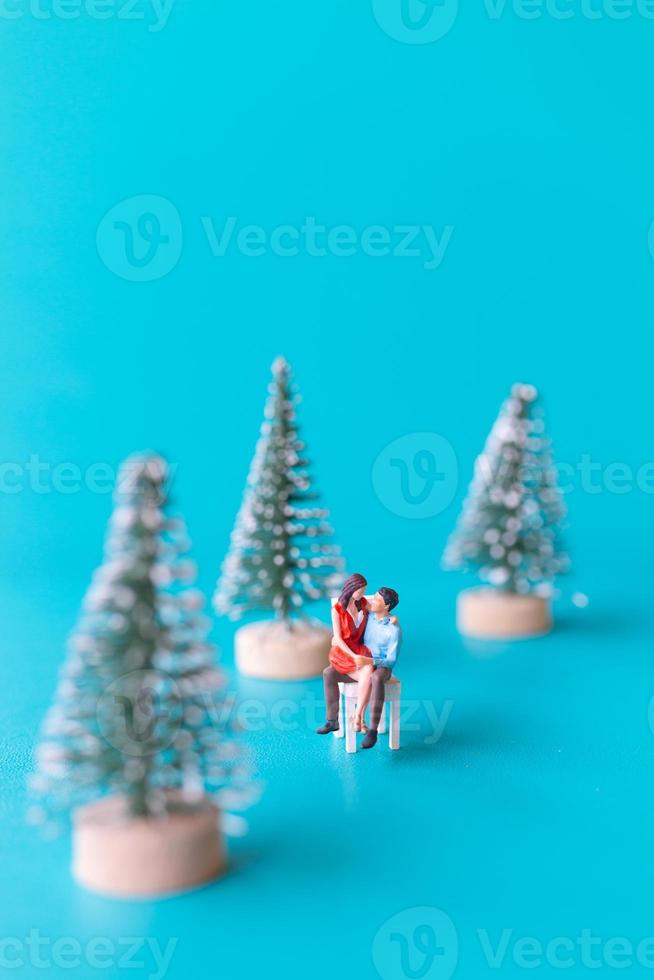 pessoas em miniatura, casal apaixonado sentado ao lado de uma árvore de natal foto