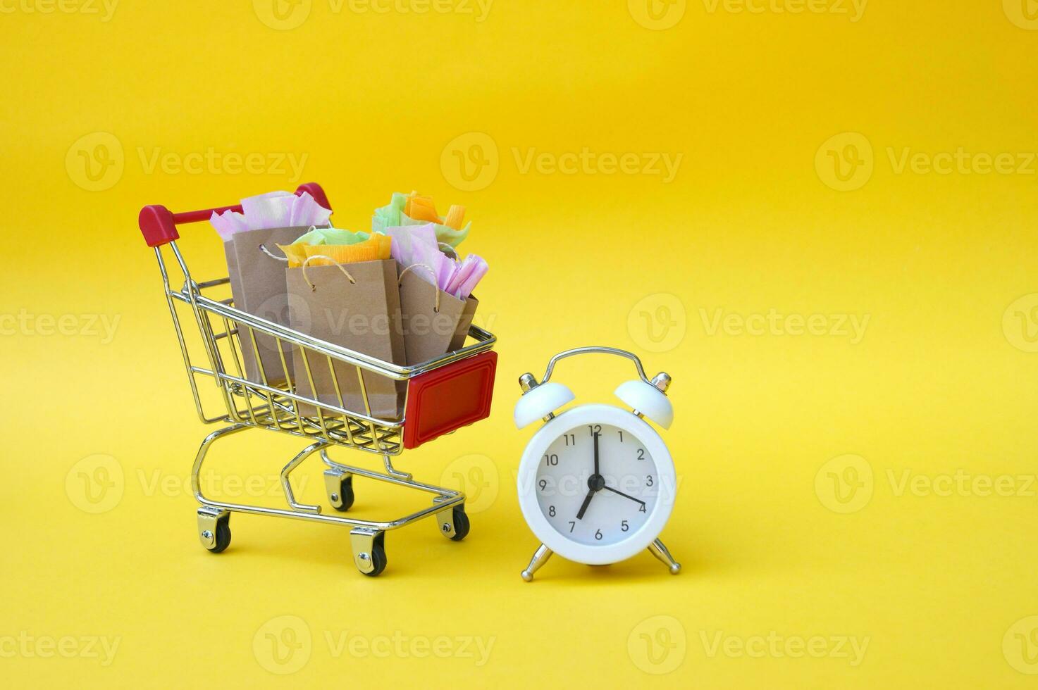 compras carrinho com papel bolsas e vintage relógio em uma amarelo fundo. foto