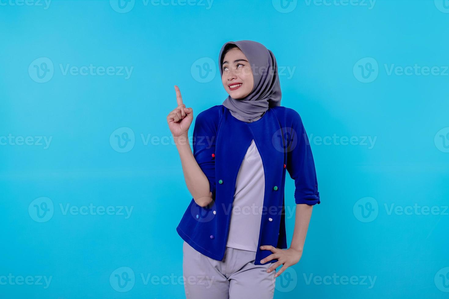 jovem carismática bonita com hijab apontando isolado em fundo azul claro foto