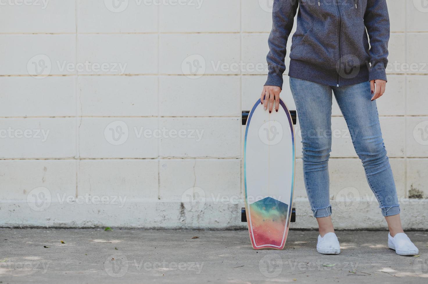mulher asiática com surfskate contra parede de concreto foto