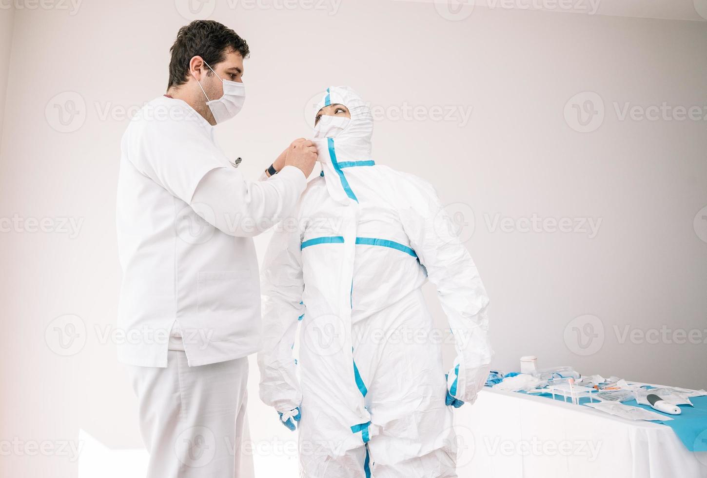 médico vestindo uniforme de proteção com ajuda de colega foto