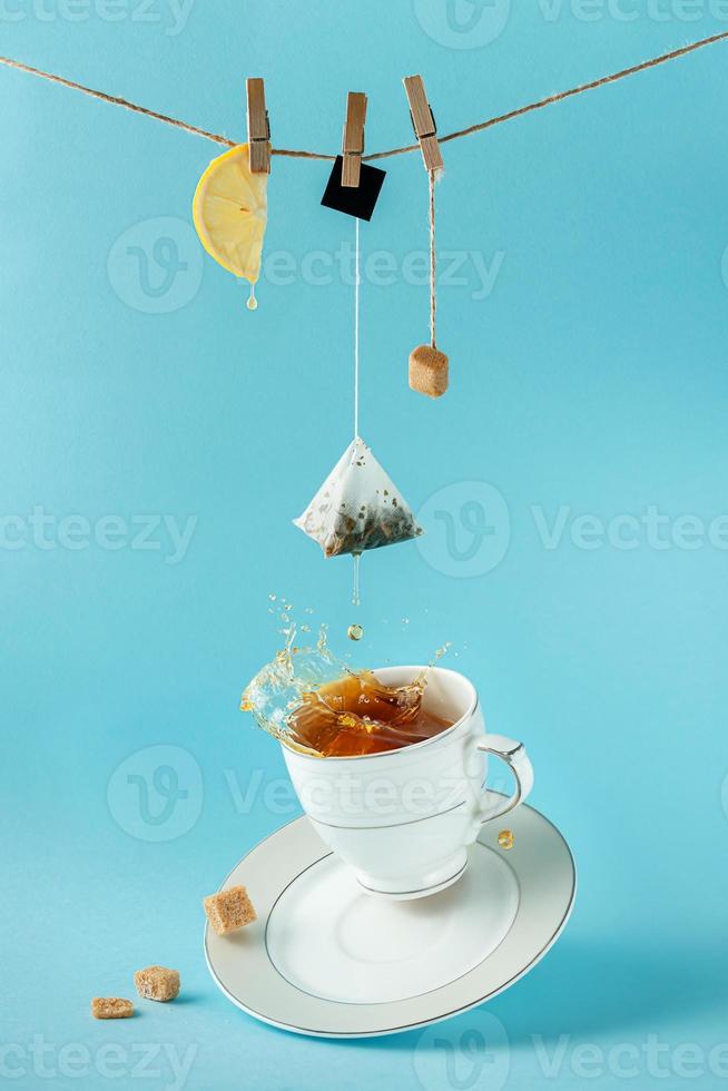 saquinho de chá, limão e açúcar pendurado na corda sobre espirrar chá no fundo azul. conceito de vida ainda criativa. foto