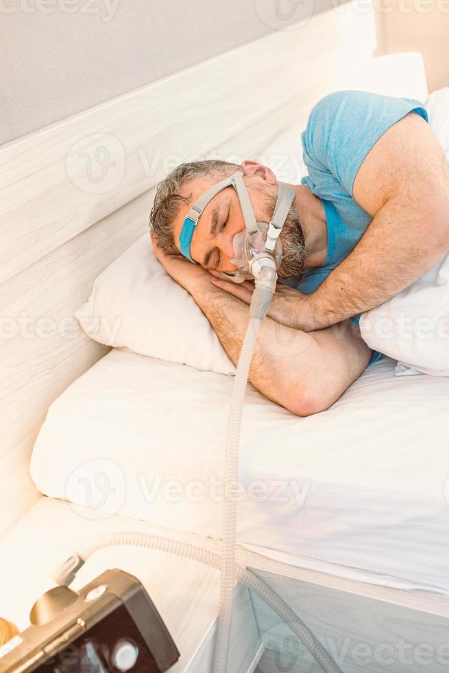 homem adormecido com problemas respiratórios crônicos considera usar máquina de cpap na cama. cuidados de saúde, terapia para apneia obstrutiva do sono, cpap, conceito de ronco foto