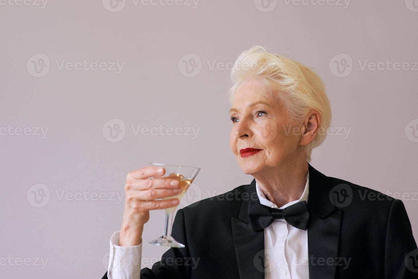 elegante sommelier maduro mulher sênior de smoking com uma taça de vinho espumante. diversão, festa, estilo, estilo de vida, álcool, conceito de celebração foto