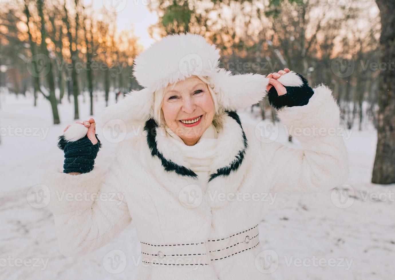 mulher sênior com chapéu branco e casaco, aproveitando o inverno no parque de neve. inverno, idade, conceito de estação foto