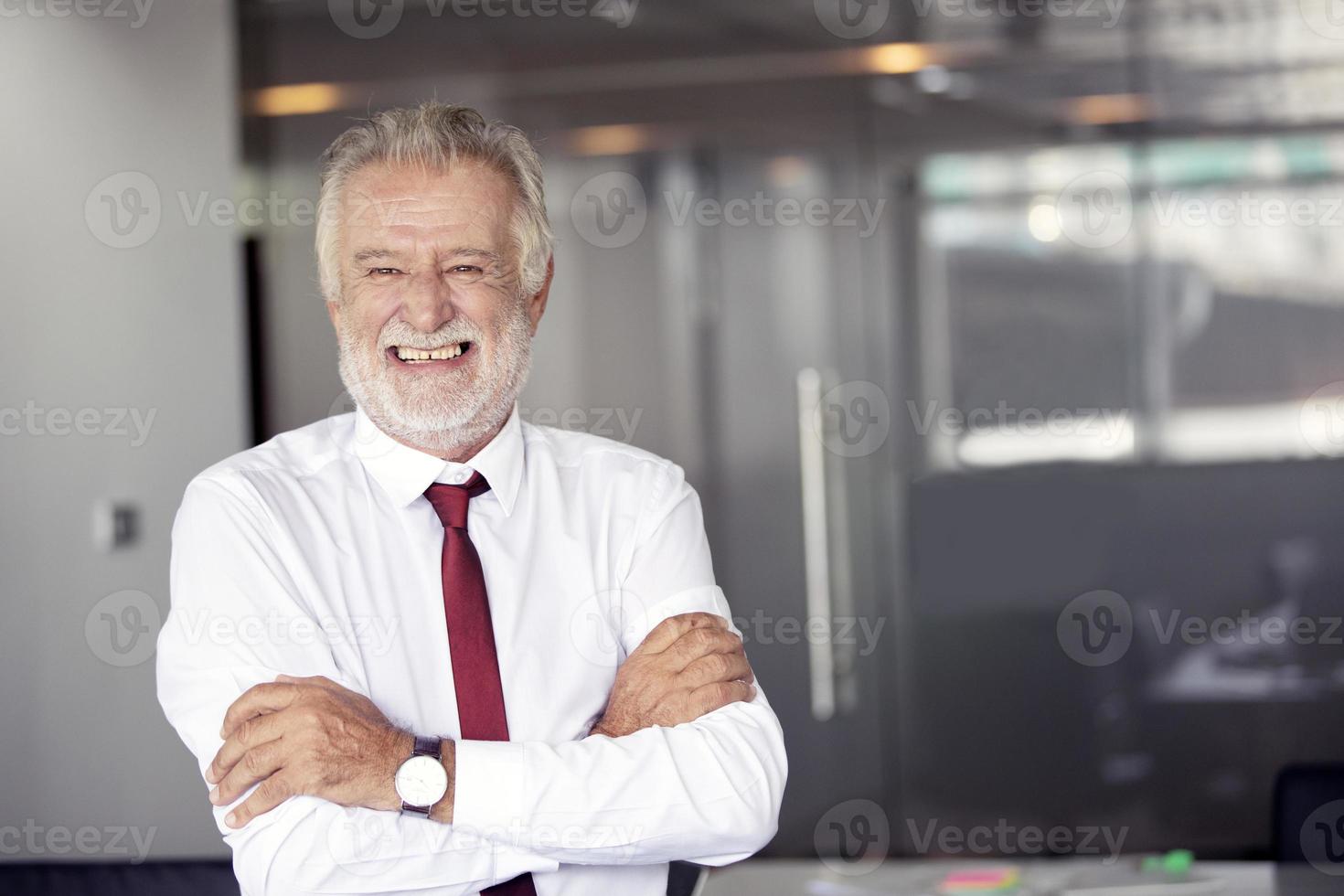 feliz bonito velho empresário em pé e sorrindo no escritório foto