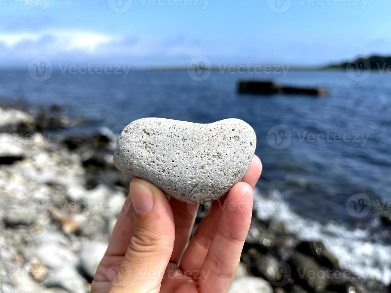 pedra de forma de coração na mão de meninas contra o fundo da praia. dia ensolarado de verão. conceito de amor, casamento e dia dos namorados. encontrar pedras bonitas e interessantes. férias na praia foto