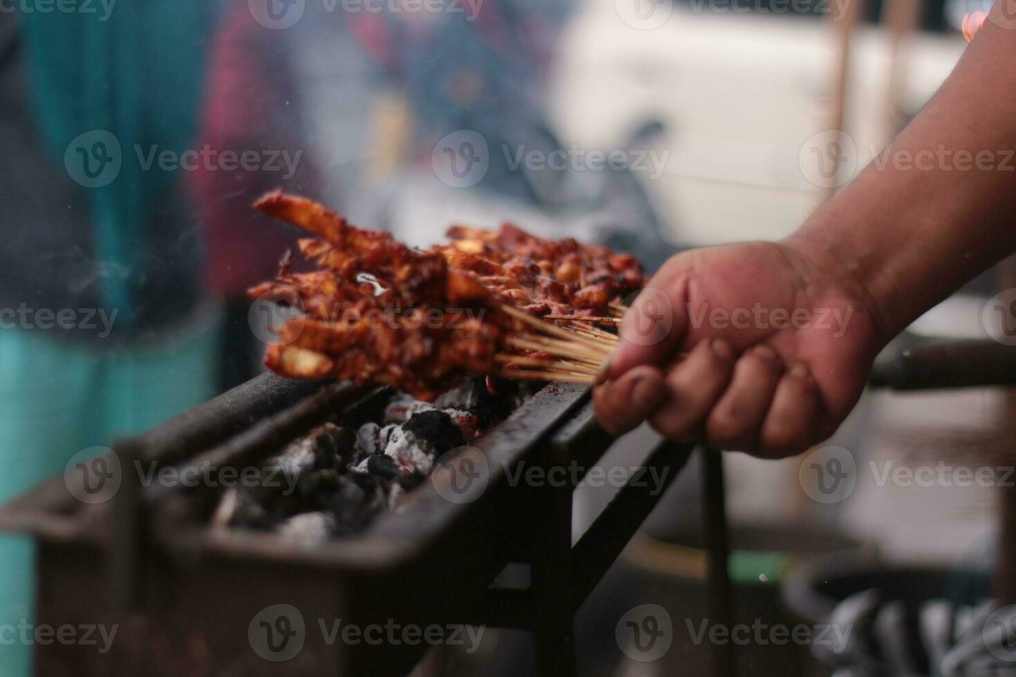 frango satay sobre tradicional carvão fogo. a satay queimaduras com fumaça e a apetitoso aparência. mãos cozinhando satay em a grade. pessoas estão já fila. foto