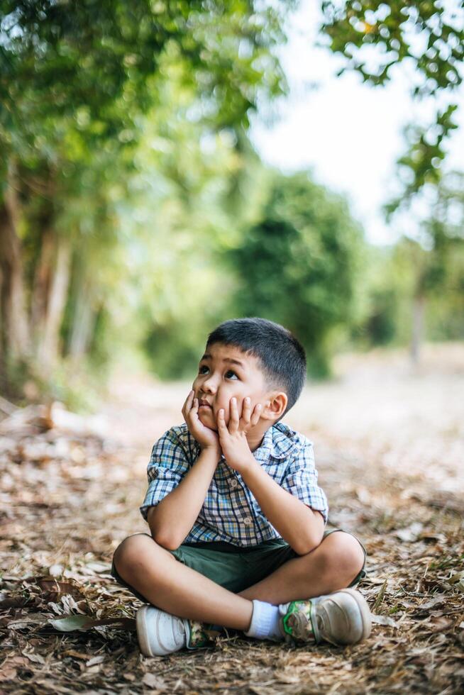 menino feliz sentado e pensando sozinho no parque foto