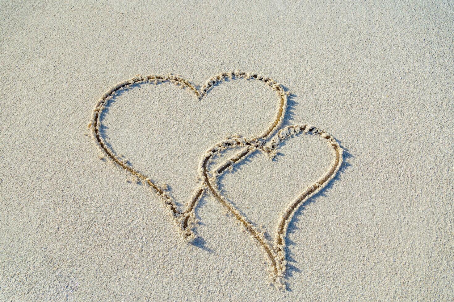 dois corações em a praia, tropical lua de mel ou aniversário. desenhando dentro areia com passos. romântico viagem conceito foto