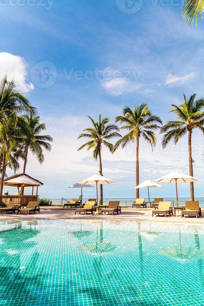 bela praia tropical e mar com guarda-sol e cadeira ao redor da piscina em hotel resort foto