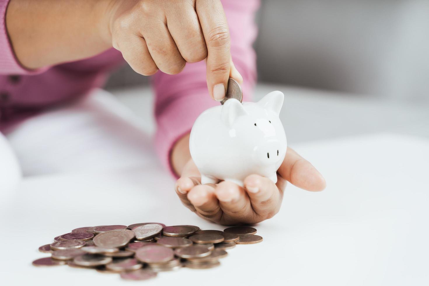 close-up da mão de uma mulher colocando moedas de dinheiro no cofrinho para economizar dinheiro. economizando dinheiro e conceito financeiro foto