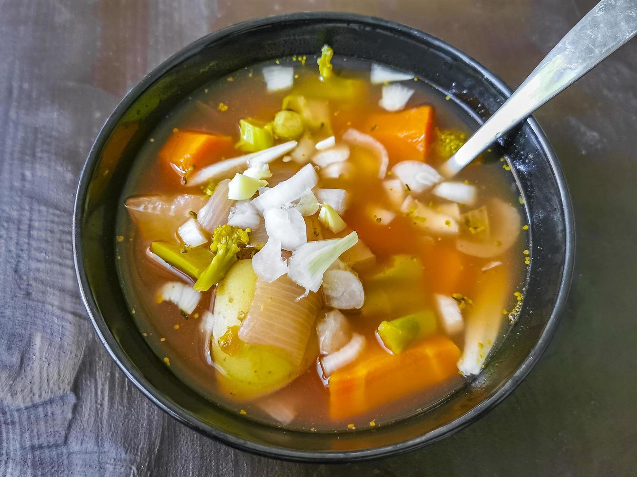 sopa de legumes com cenoura batata cebola brócolis em tigela preta foto