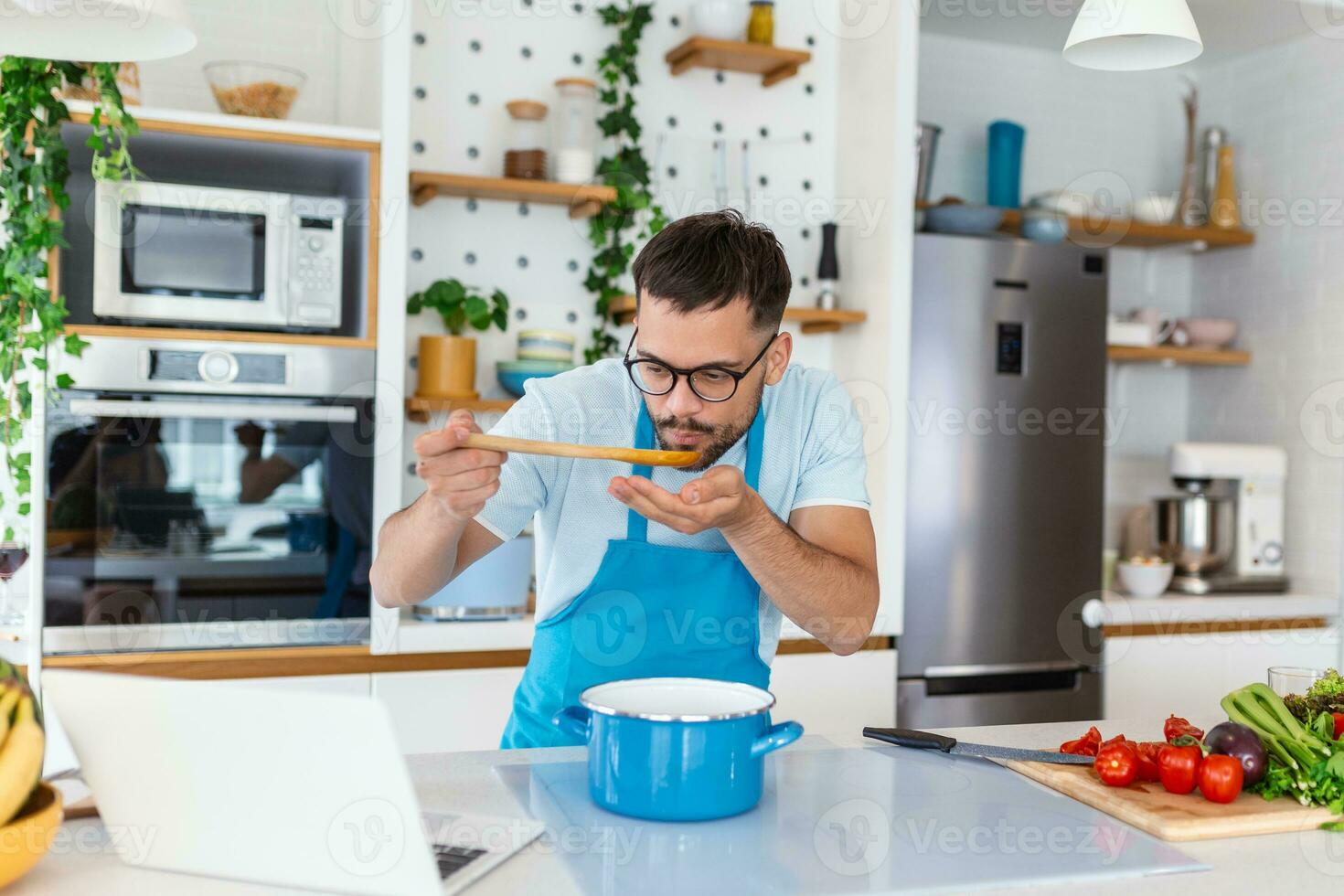 jovem sorridente homem desfrutando dentro gosto e cheiro enquanto cozinhando almoço dentro a cozinha. foto