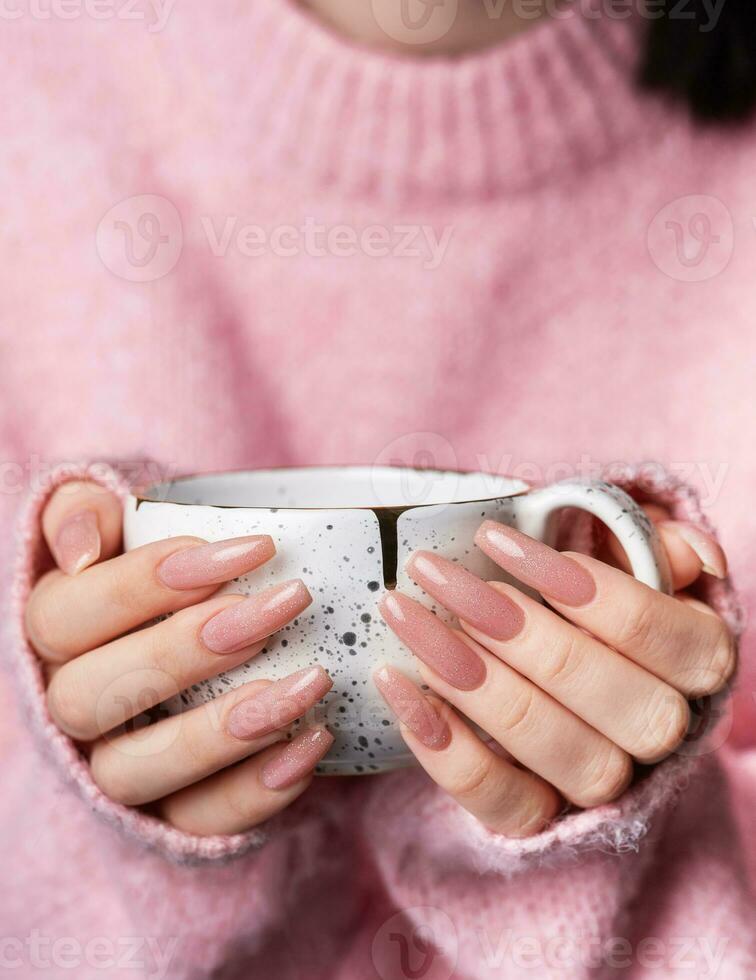 mulher dentro uma Rosa suéter com uma Rosa manicure detém uma copo com quente café foto