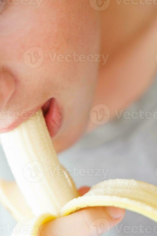 retrato do uma Adolescência Garoto comendo uma banana. foto do uma pessoal boca e lábios com uma banana. fresco fruta. saudável alimentos para crianças
