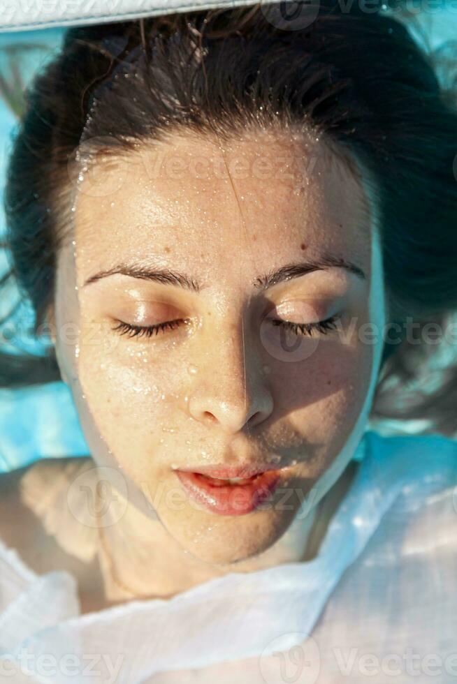 retrato do jovem menina dentro roupa de banho flutuando em azul água do natação piscina dentro luz solar foto