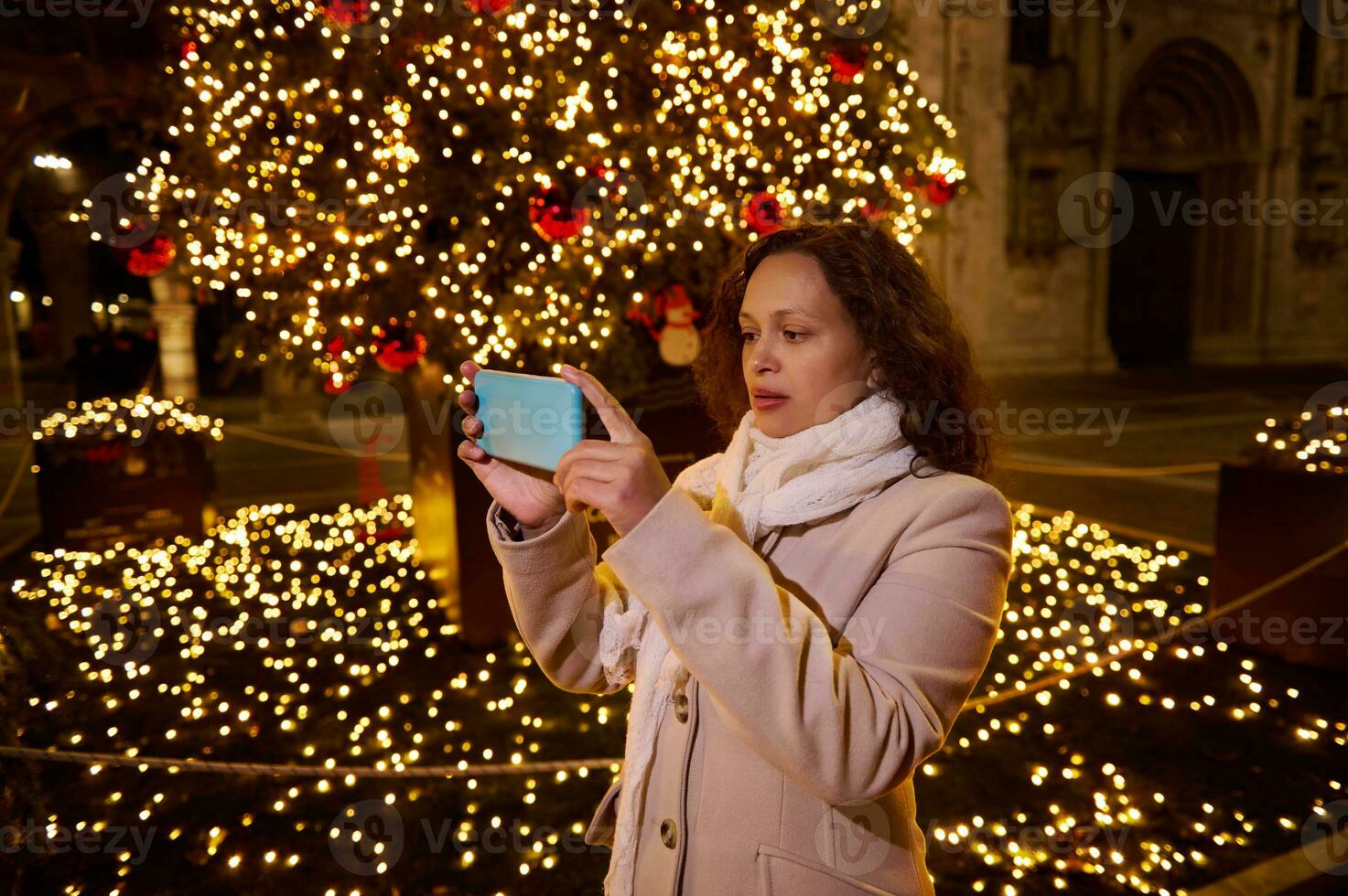 lindo encaracolado cabelos morena mulher fotografando a Natal feira dentro a cidade quadrado às noite foto