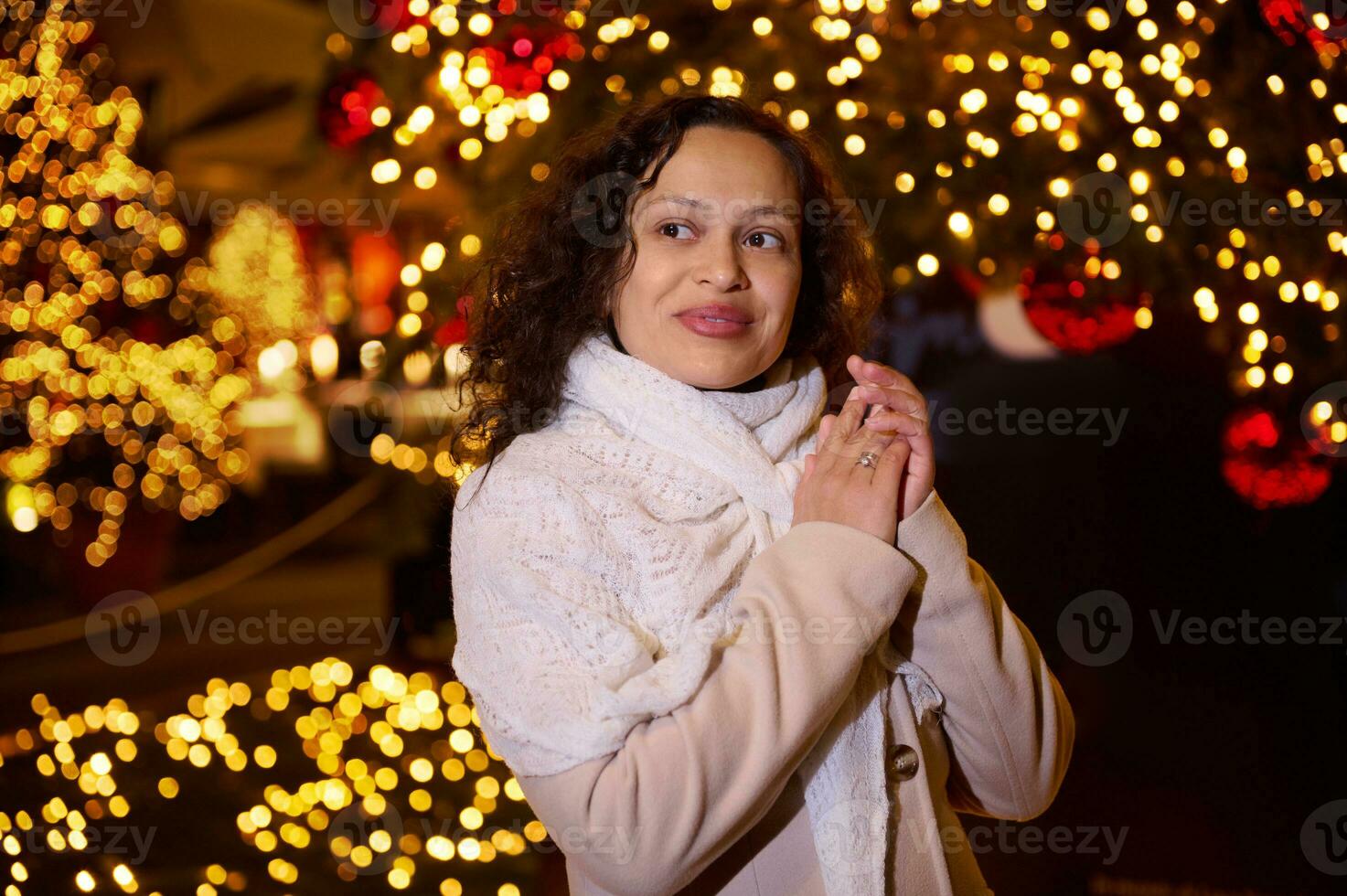 sorridente feliz mulher caminhando dentro Natal mercado decorado com feriado luzes dentro a tarde. sentindo-me feliz dentro grande cidade. foto
