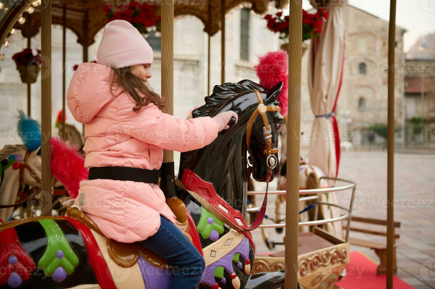 pequeno criança menina equitação uma de madeira cavalo em uma carrossel às Natal parque de diversões. foto