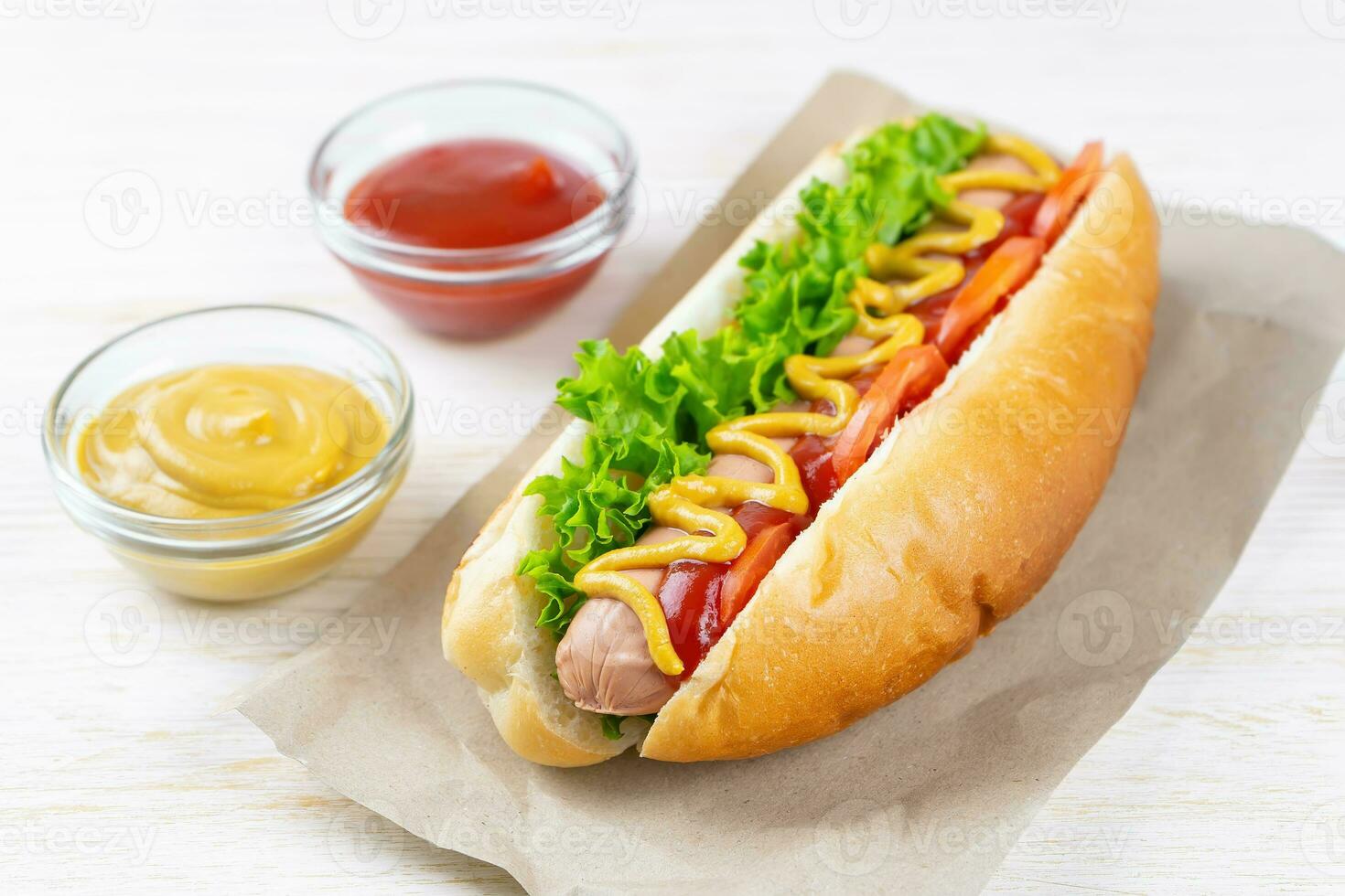 caseiro quente cachorro com mostarda, ketchup, tomate e fresco salada folhas em branco de madeira fundo foto