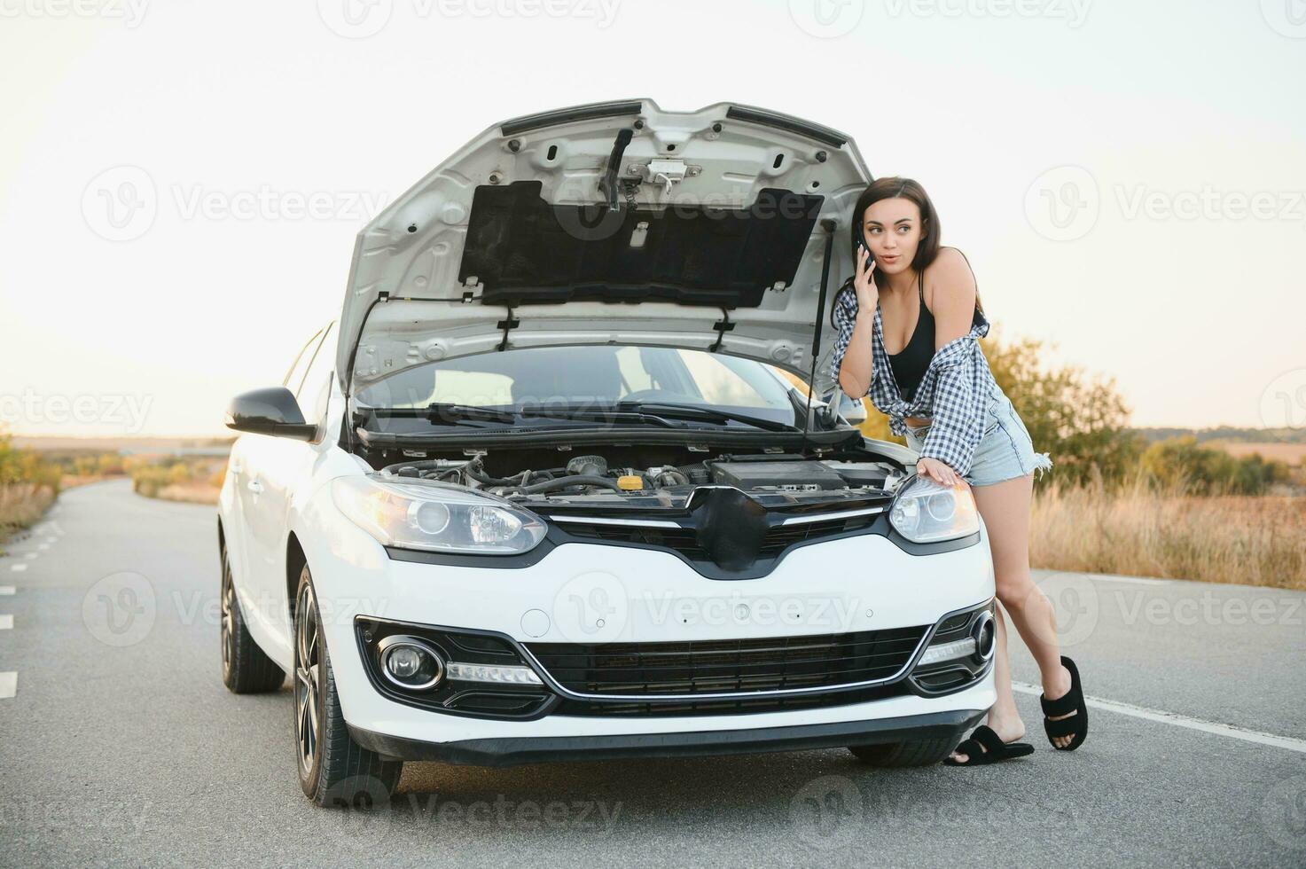atraente fino jovem menina dentro verão calção e camisa reparos uma quebrado carro. uma lindo mulher carrinhos perto elevado carro capuz. foto