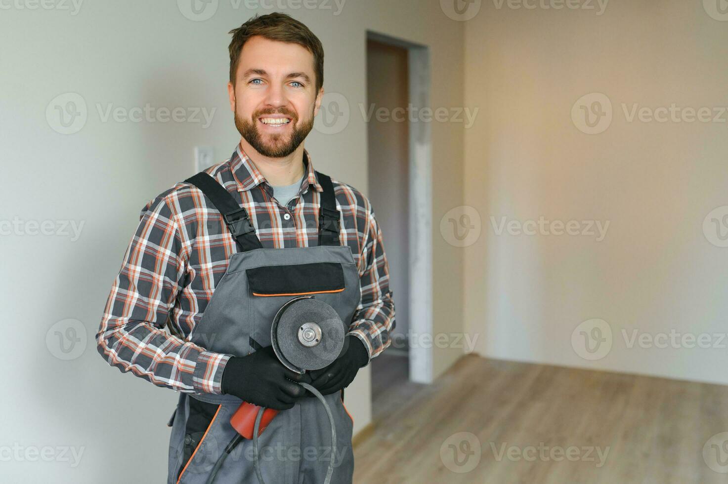 retrato do uma confiante reparador com barba em pé dentro esvaziar apartamento foto