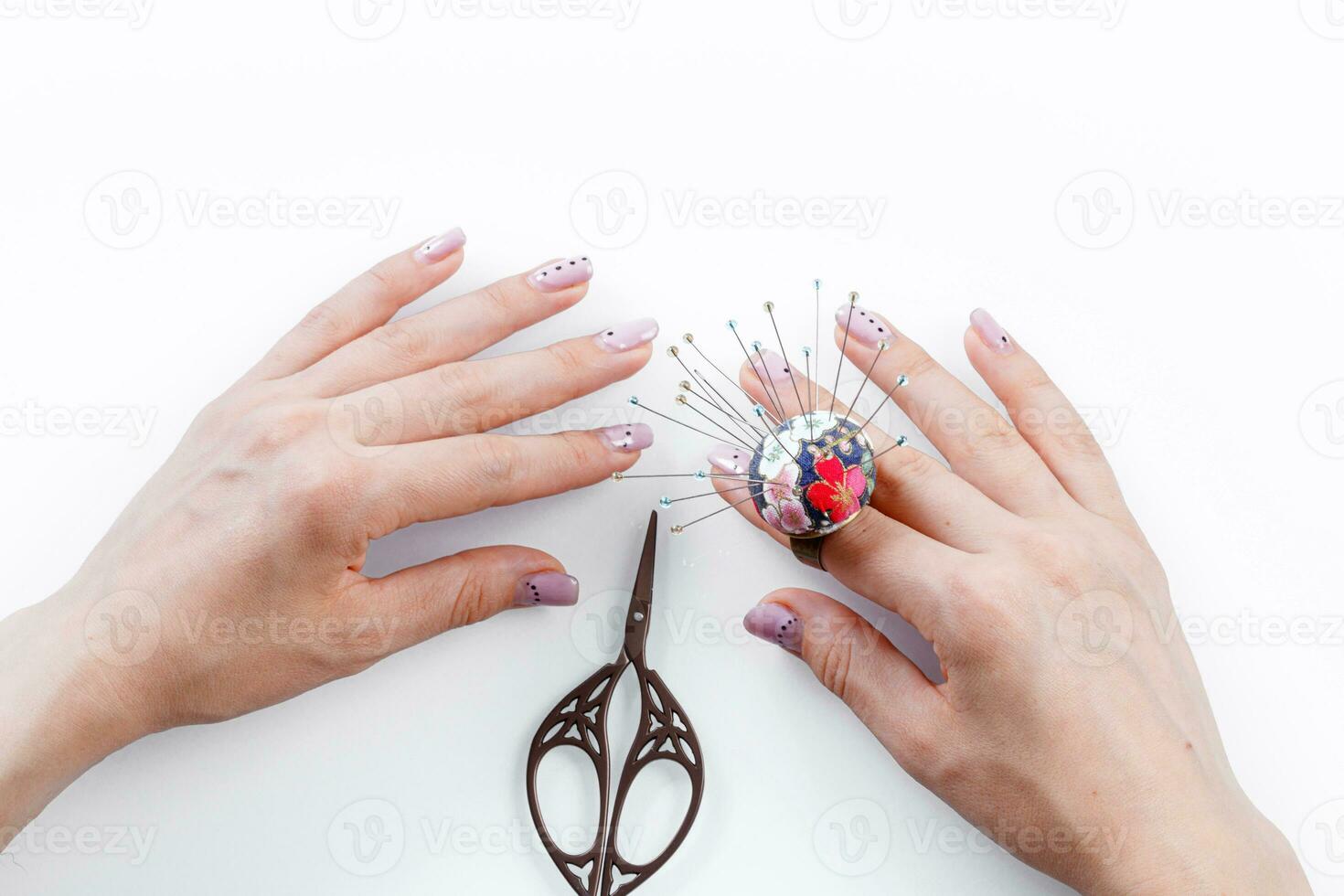uma anel com uma pequeno travesseiro para agulhas em uma mão e tesouras em uma branco fundo foto