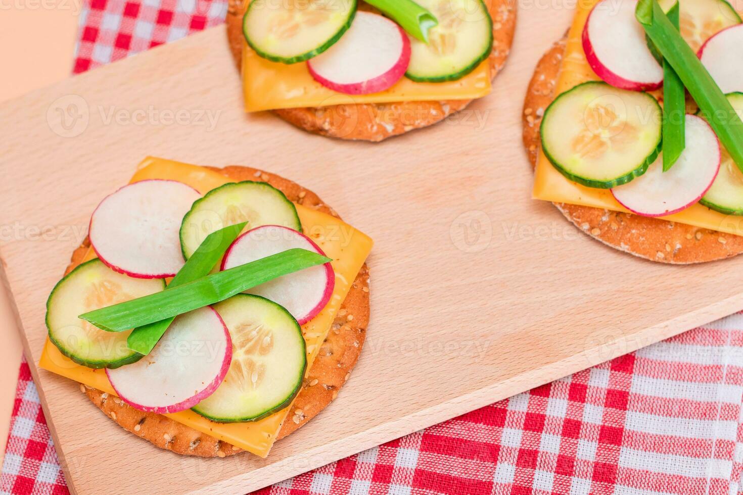 luz café da manhã. rápido e saudável sanduíche. fresco pepino e rabanete com verde cebolas e queijo em crocantes biscoito em de madeira corte borda foto