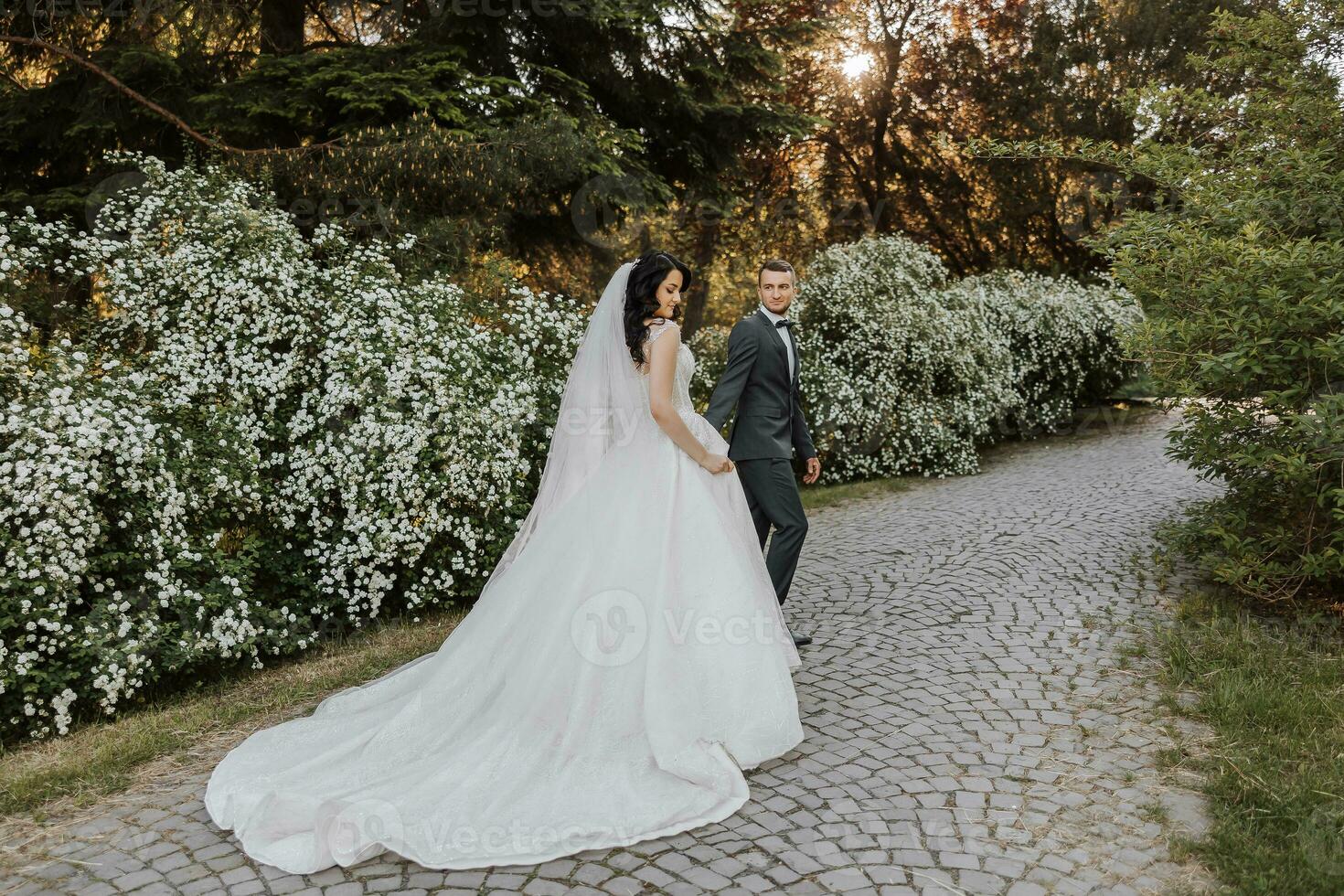 feliz jovem casal, noiva com grandes encaracolado cabelo dentro branco vestir com grandes trem perto castelo dentro lindo flores lindo menina dentro a parque. lindo luz solar. Casamento foto tiro