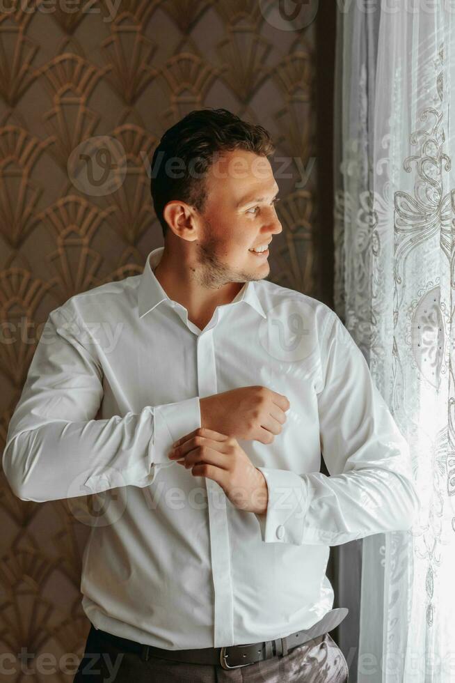 retrato do uma elegante homem fixação à moda abotoaduras em a mangas do dele branco camisa. Casamento dia conceito. foto