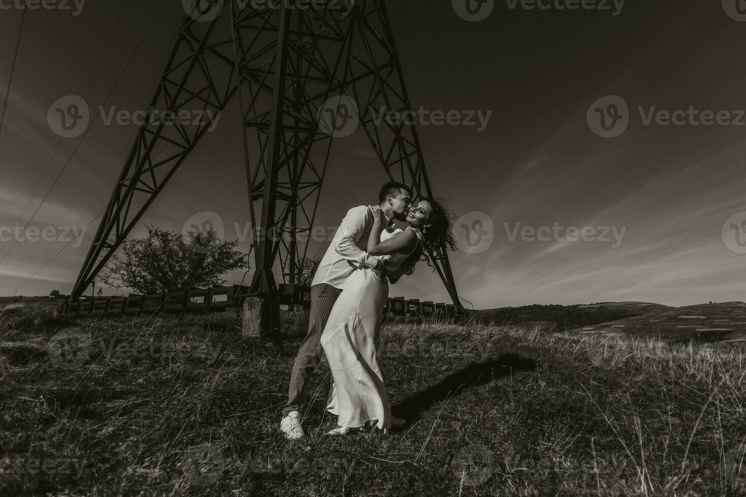 à moda modelo casal dentro a montanhas dentro verão. uma jovem Garoto e menina dentro uma branco seda vestir estão em pé perto ampla estruturas do poder linhas. Preto e branco contraste foto