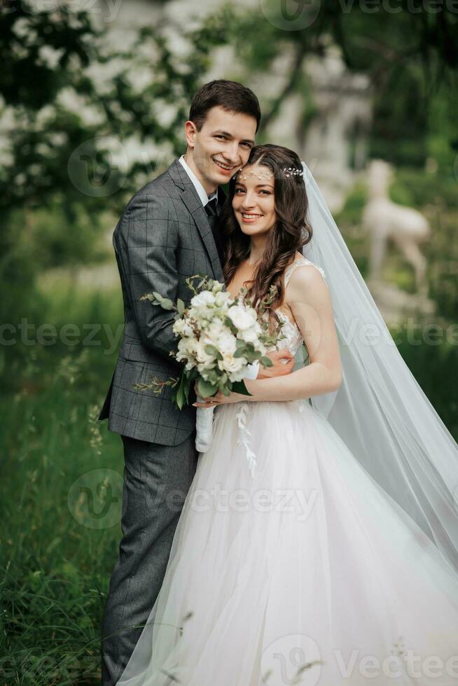 feliz jovem casal. Casamento retrato. a noiva ternamente abraçado a noivo. jovem noivas e noivos estão ternamente abraçando enquanto olhando às a Câmera. Casamento ramalhete. Primavera Casamento foto