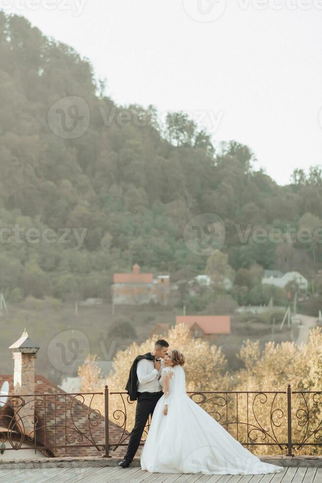 Casamento retrato. a noivo dentro uma Preto terno e a Loiras noiva estão de pé, abraçando, posando segurando uma ramalhete debaixo uma árvore. foto sessão dentro natureza. lindo cabelo e Maquiagem