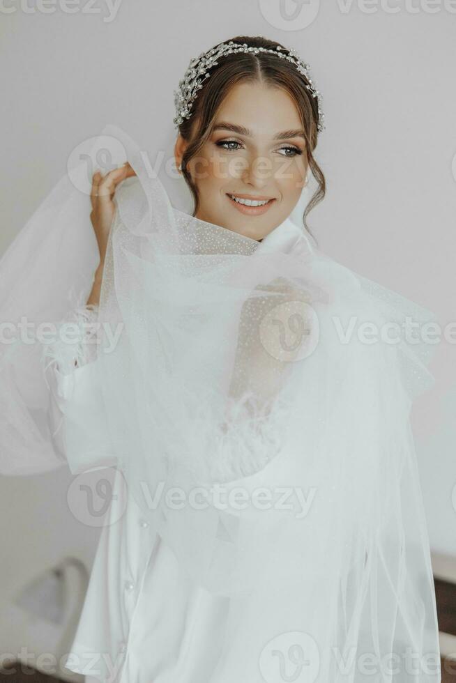manhã do noiva antes a casamento. lindo jovem mulher com grandes véu dentro uma branco manto. natural beleza e profissional maquiagem.menina dentro branco renda boudoir vestir. foto