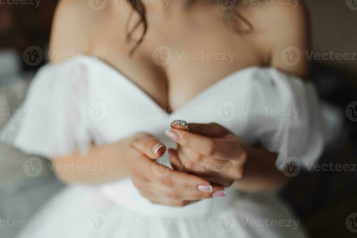 uma morena noiva dentro uma branco vestir detém dela prata Casamento anel. francês manicure. aberto ombros. lindo mãos. grandes véu. manhã do a noiva. detalhes foto