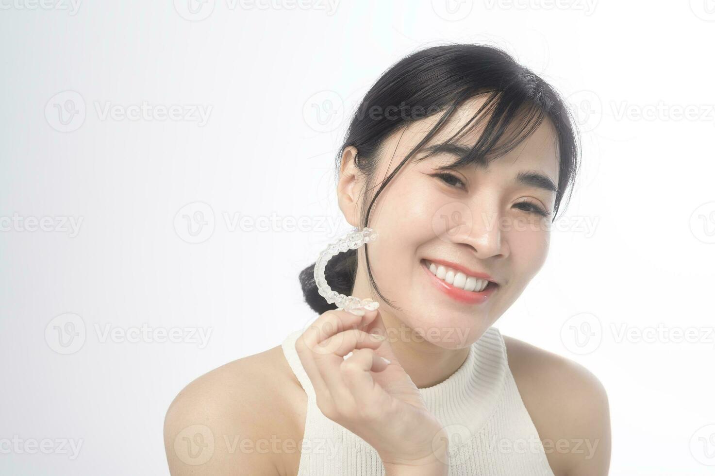 jovem mulher sorridente segurando aparelho invisalign sobre estúdio de fundo branco, saúde bucal e conceito ortodôntico. foto