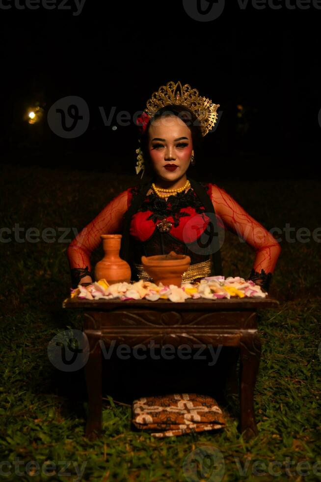 a ásia mulher dentro uma vermelho dançarina vestir é sentado às uma ritual oferta mesa cheio do flores foto