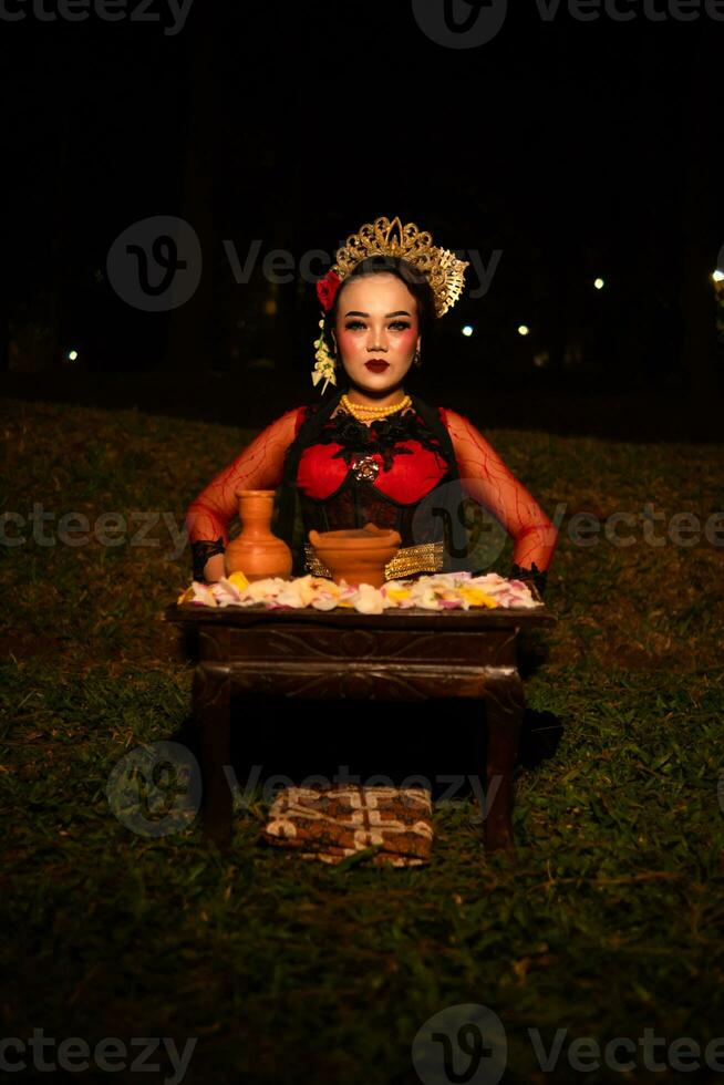 Largo tiro do a ásia menina dentro tradicional roupas sentado dentro uma floresta com uma mesa cheio do flores foto