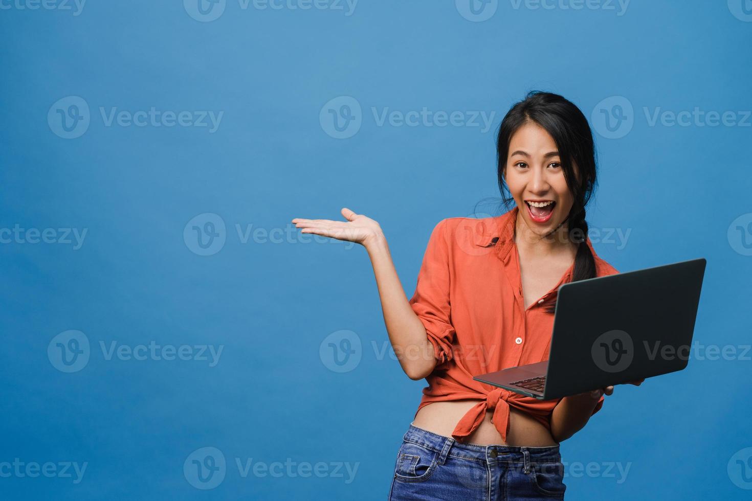 jovem asiática usando laptop com expressão positiva, sorri amplamente, vestida com roupas casuais, sentindo felicidade e carrinho isolado sobre fundo azul. feliz adorável feliz mulher alegra sucesso. foto