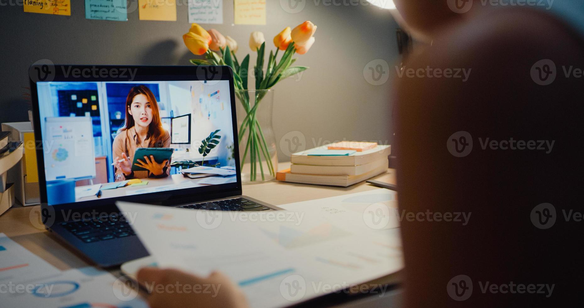 empresária asiática usando laptop conversa com colegas sobre o plano de uma reunião de videochamada na sala de estar em casa. trabalho em casa sobrecarregada à noite, remotamente, distância social, quarentena para coronavírus. foto